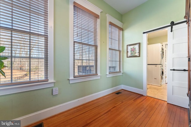 empty room with hardwood / wood-style flooring, a barn door, and stacked washing maching and dryer