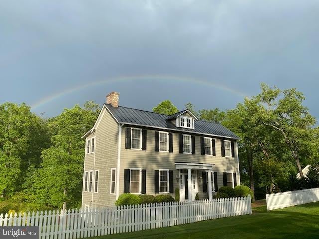 colonial inspired home featuring a fenced front yard, a chimney, metal roof, a standing seam roof, and a front lawn