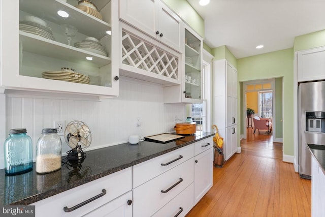 kitchen with dark stone countertops, stainless steel fridge, light hardwood / wood-style floors, and white cabinets