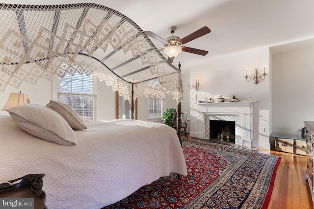 bedroom featuring hardwood / wood-style flooring, a premium fireplace, and ceiling fan