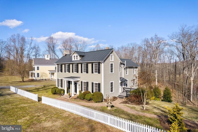 exterior space with a fenced front yard, a chimney, a lawn, a standing seam roof, and metal roof