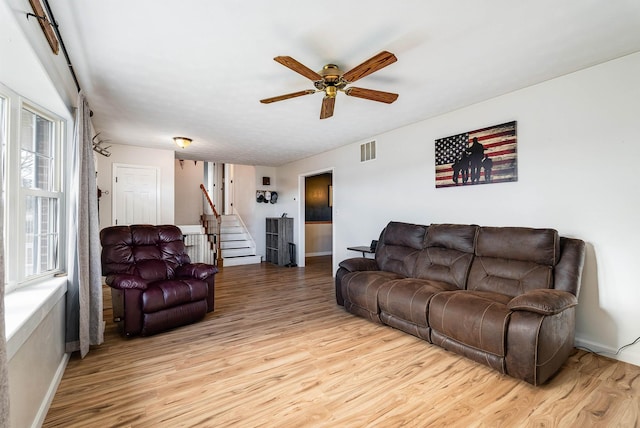 living room featuring light wood-style flooring, visible vents, ceiling fan, and stairway