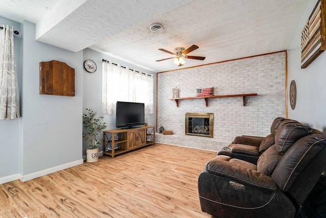 living room with light wood finished floors, baseboards, visible vents, ceiling fan, and a brick fireplace