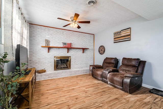 living area with a textured ceiling, wood finished floors, visible vents, a ceiling fan, and a brick fireplace