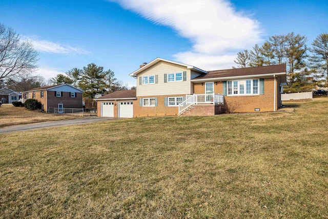 split level home featuring driveway, brick siding, an attached garage, fence, and a front yard