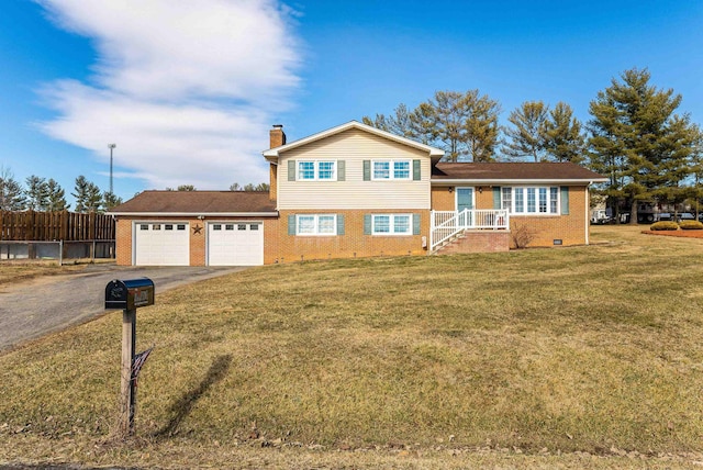 tri-level home featuring brick siding, a chimney, a front yard, a garage, and driveway