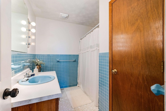 full bathroom with visible vents, wainscoting, tile patterned flooring, vanity, and tile walls