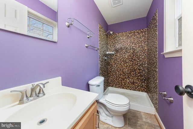 bathroom featuring vanity, a tile shower, and toilet