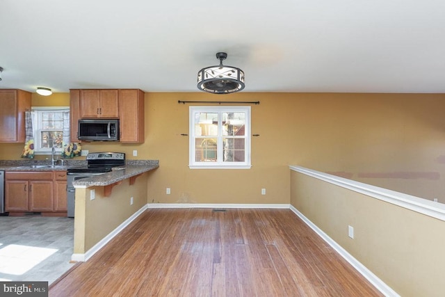 kitchen with sink, appliances with stainless steel finishes, a kitchen bar, decorative light fixtures, and light wood-type flooring