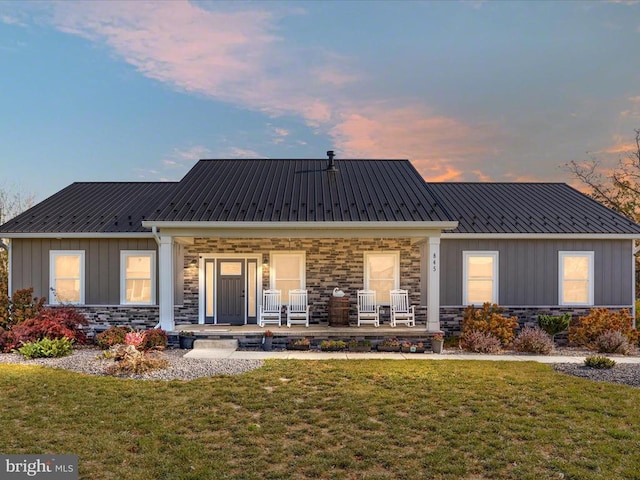 back house at dusk featuring a yard and covered porch