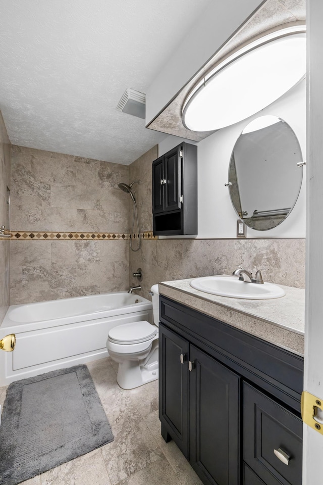 full bathroom with toilet, tile walls, a textured ceiling, vanity, and tiled shower / bath combo