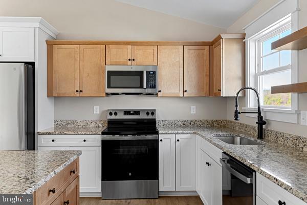 kitchen featuring vaulted ceiling, appliances with stainless steel finishes, white cabinetry, sink, and light stone counters