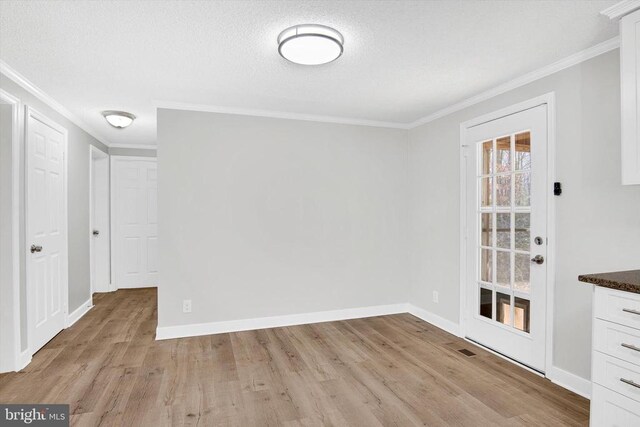 unfurnished dining area featuring ornamental molding, a textured ceiling, and light wood-type flooring