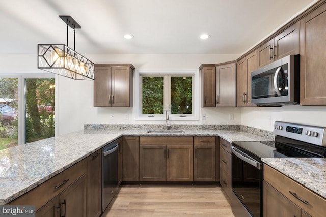 kitchen featuring pendant lighting, sink, kitchen peninsula, stainless steel appliances, and light stone countertops