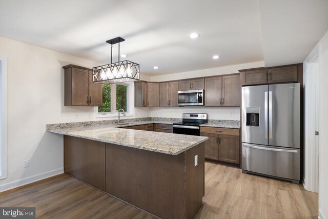 kitchen with appliances with stainless steel finishes, kitchen peninsula, sink, and hanging light fixtures