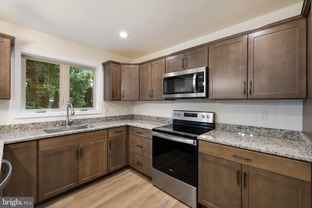 kitchen featuring sink, light stone counters, dark brown cabinets, light wood-type flooring, and stainless steel appliances