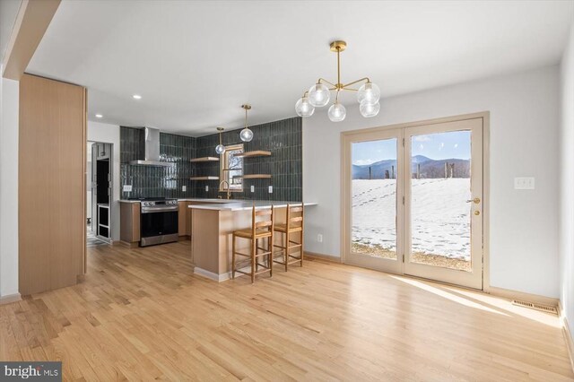 kitchen with stainless steel range oven, a breakfast bar area, hanging light fixtures, kitchen peninsula, and wall chimney range hood