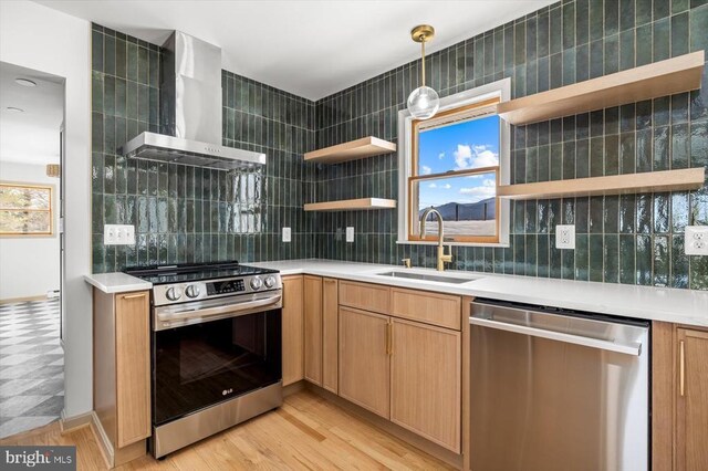 kitchen featuring wall chimney range hood, sink, stainless steel appliances, tasteful backsplash, and decorative light fixtures