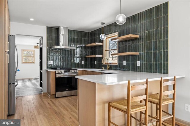 kitchen featuring wall chimney exhaust hood, a breakfast bar, decorative light fixtures, kitchen peninsula, and stainless steel appliances