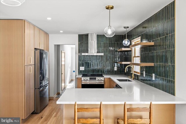 kitchen featuring sink, hanging light fixtures, kitchen peninsula, stainless steel appliances, and wall chimney exhaust hood