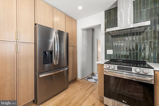 kitchen featuring light brown cabinets, appliances with stainless steel finishes, light hardwood / wood-style floors, decorative backsplash, and wall chimney range hood