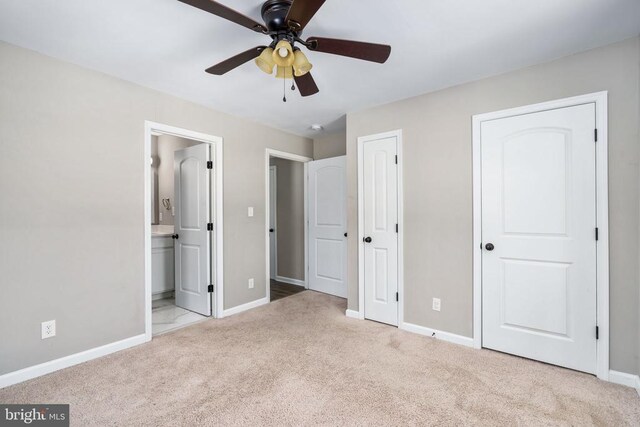 unfurnished bedroom with ensuite bathroom, two closets, light carpet, and ceiling fan