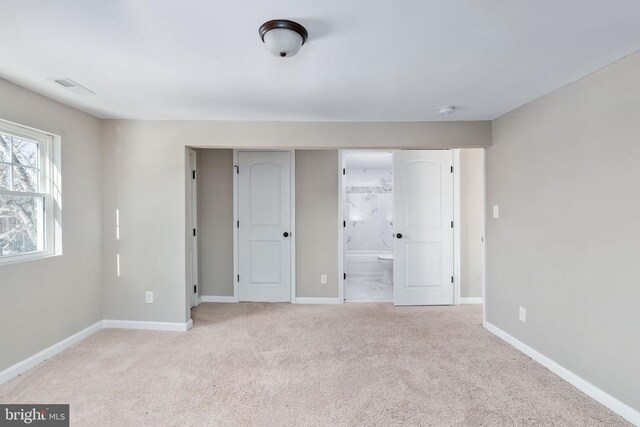 unfurnished bedroom with light carpet and connected bathroom