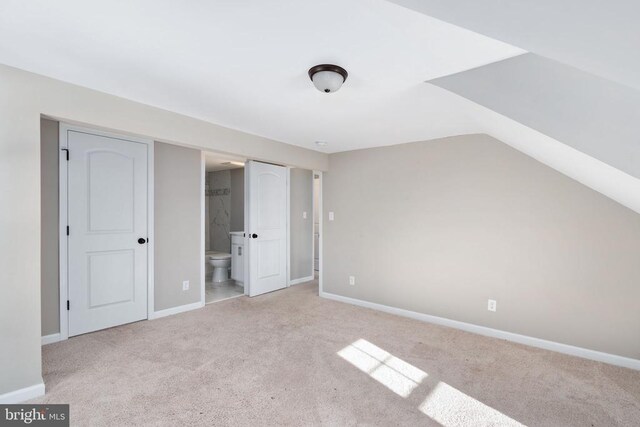 interior space with vaulted ceiling, light colored carpet, and ensuite bathroom