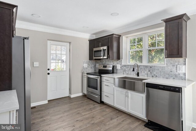 kitchen featuring sink, white cabinets, stainless steel appliances, crown molding, and light wood-type flooring