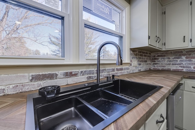 interior details with sink, wooden counters, dishwasher, tasteful backsplash, and white cabinets