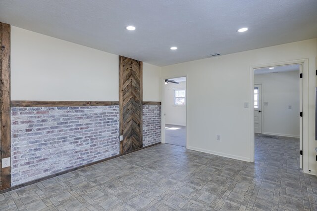 spare room featuring ceiling fan, brick wall, and a textured ceiling