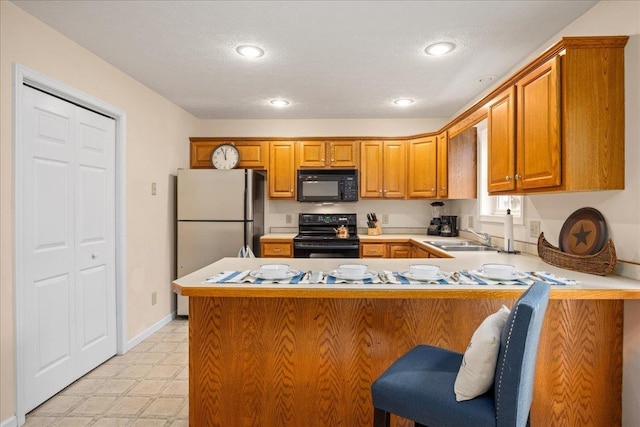 kitchen with sink, a breakfast bar area, black appliances, a textured ceiling, and kitchen peninsula