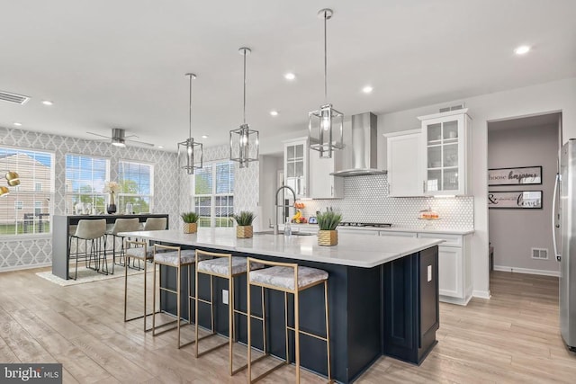 kitchen featuring a sink, wall chimney range hood, light wood finished floors, and visible vents