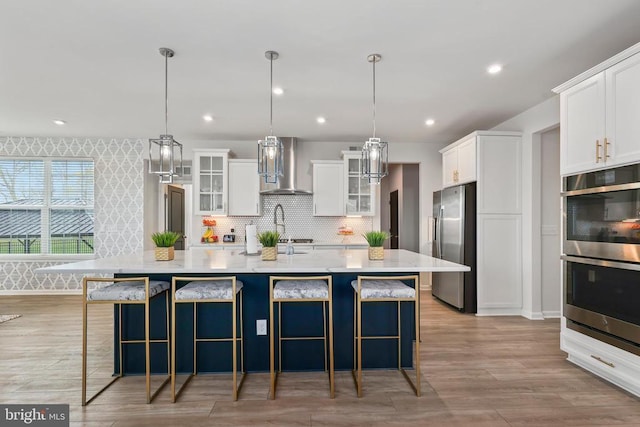 kitchen featuring wall chimney range hood, stainless steel appliances, white cabinetry, and a spacious island