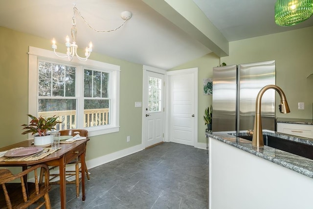 kitchen with lofted ceiling with beams, dark stone countertops, white cabinets, stainless steel fridge, and an inviting chandelier