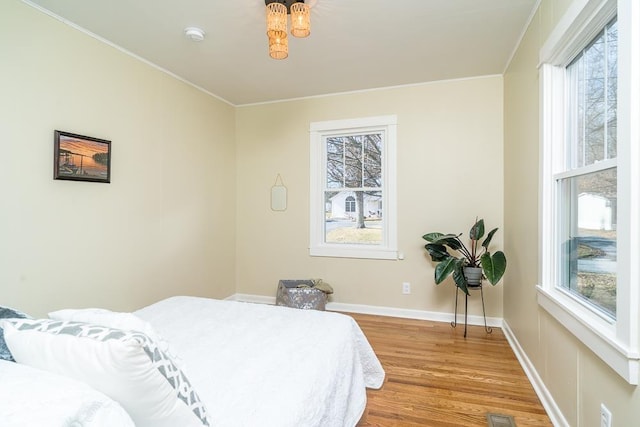 bedroom with multiple windows, ornamental molding, and light hardwood / wood-style flooring