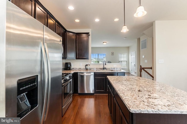 kitchen with sink, a center island, hanging light fixtures, stainless steel appliances, and light stone countertops