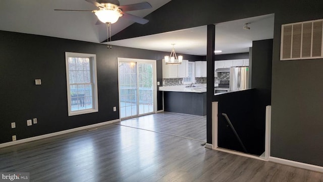 kitchen featuring white cabinetry, decorative light fixtures, vaulted ceiling, light wood-type flooring, and stainless steel refrigerator