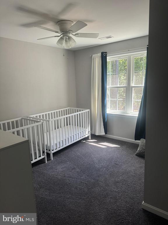 unfurnished bedroom with dark carpet, a crib, and ceiling fan