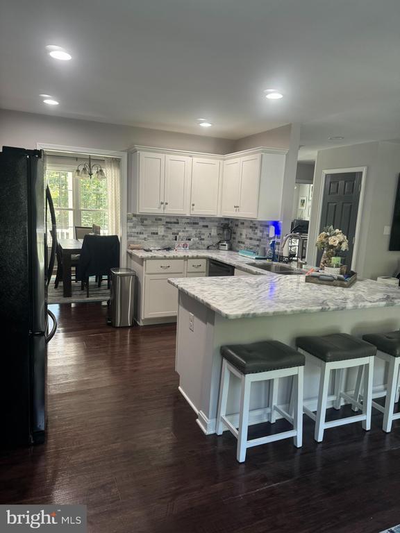 kitchen with sink, black refrigerator, a kitchen breakfast bar, light stone countertops, and white cabinets