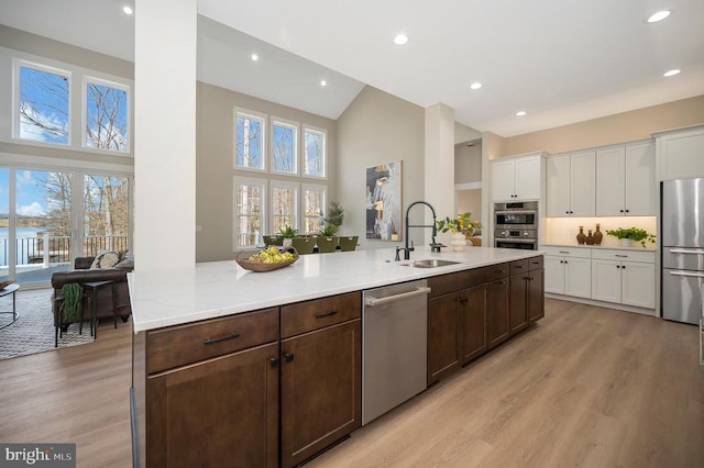 kitchen with dark brown cabinetry, white cabinets, stainless steel appliances, light wood-type flooring, and a sink