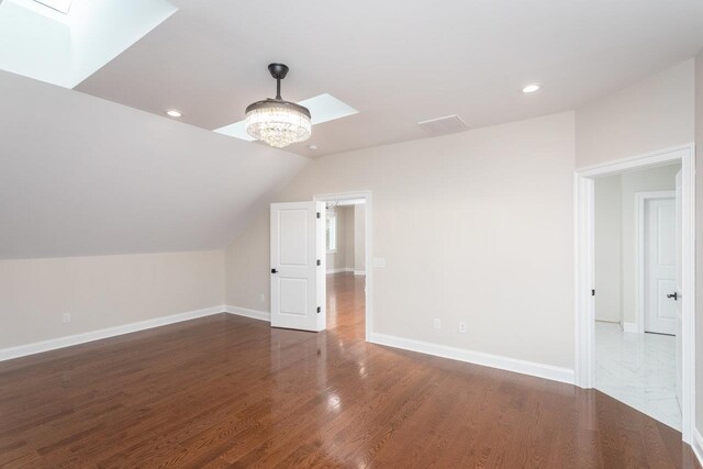 additional living space featuring lofted ceiling with skylight, dark hardwood / wood-style floors, and a chandelier