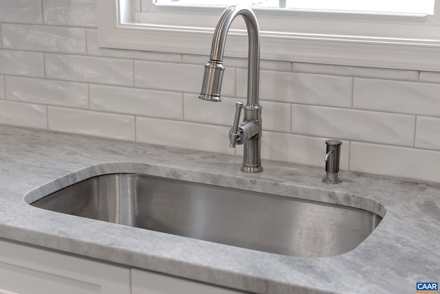 interior details featuring white cabinetry, light stone countertops, sink, and backsplash