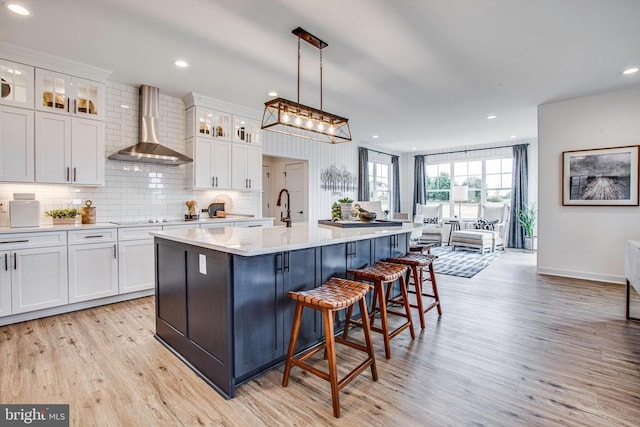 kitchen featuring white cabinets, decorative light fixtures, wall chimney exhaust hood, and a center island with sink