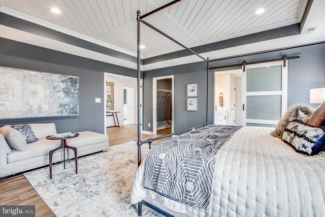 bedroom with ensuite bathroom, a walk in closet, wooden ceiling, a barn door, and hardwood / wood-style floors