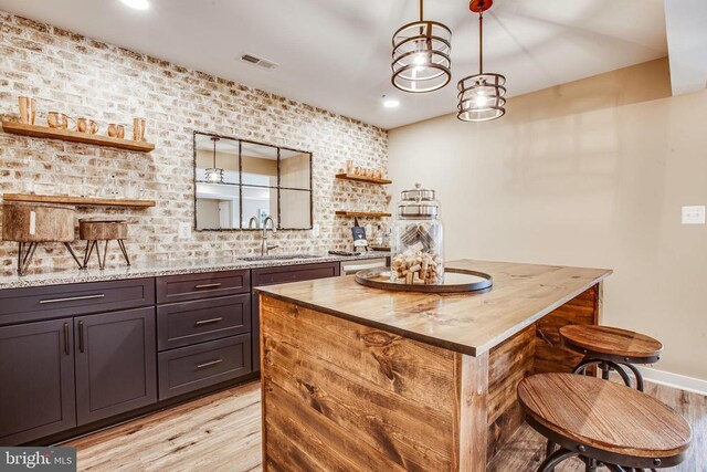 kitchen featuring sink, light hardwood / wood-style flooring, dark brown cabinets, a center island, and light stone counters