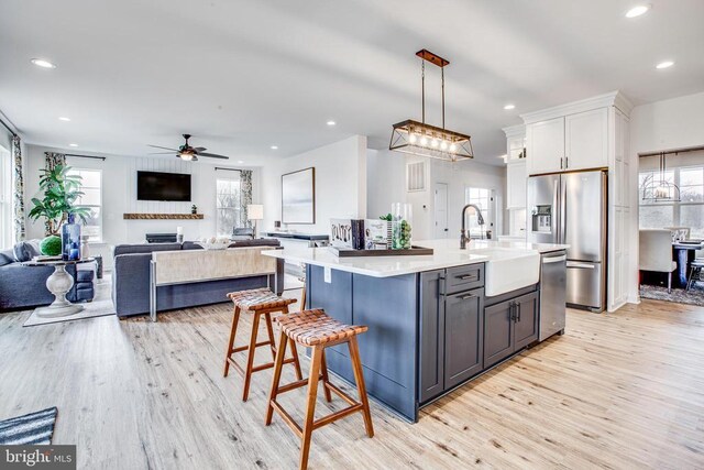 kitchen with appliances with stainless steel finishes, decorative light fixtures, sink, white cabinets, and a center island with sink