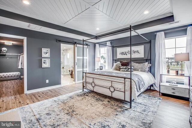 bedroom featuring a spacious closet, light hardwood / wood-style floors, a barn door, and wooden ceiling