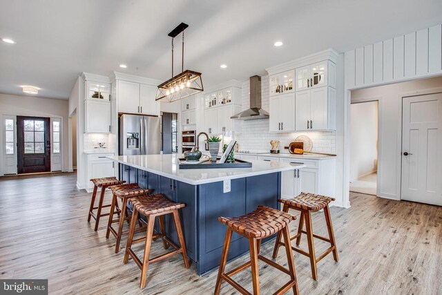 kitchen with pendant lighting, white cabinets, stainless steel appliances, and wall chimney exhaust hood