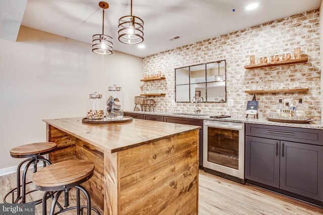 bar with gray cabinets, sink, beverage cooler, light stone countertops, and light hardwood / wood-style flooring